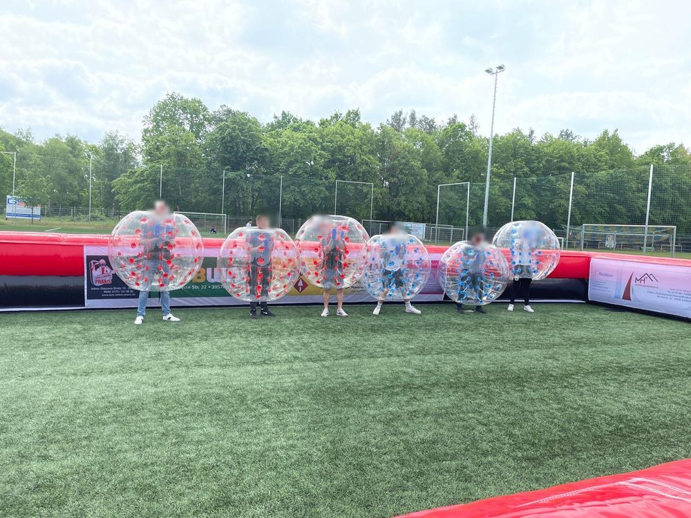 Sechs Spieler in aufblasbaren Bubble Balls auf einem Spielfeld mit Bande